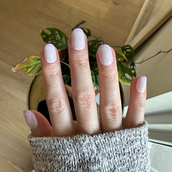 Tonal Lavender French | Extra Short | Round - Tab Press-On nails with soft lavender French tips on hand indoors against plant background
